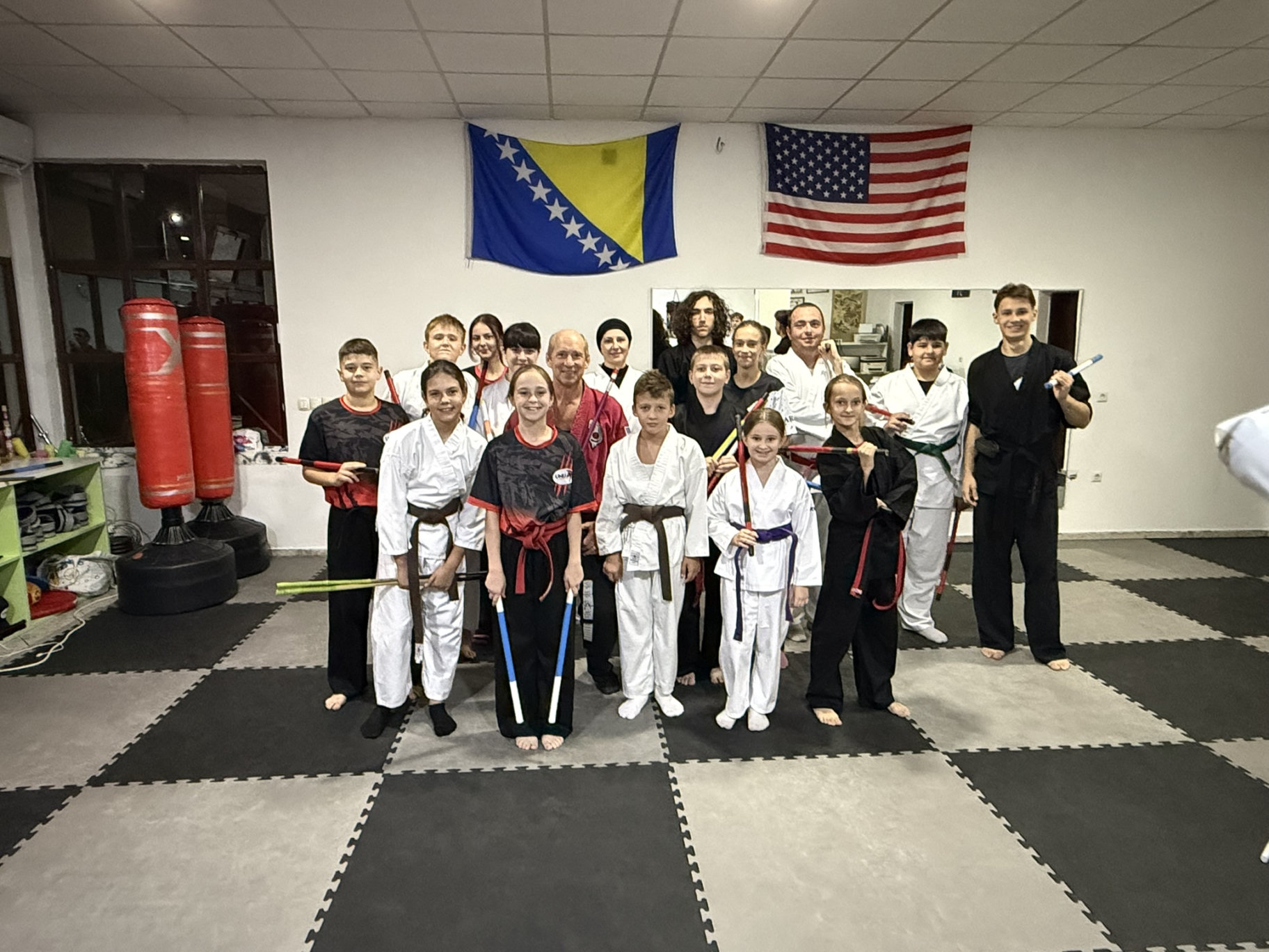 Martial arts students and instructors together in a dojo in Bosnia, beneath the Bosnian and American flags